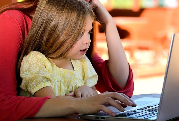 A young girl learning on laptop with a parent