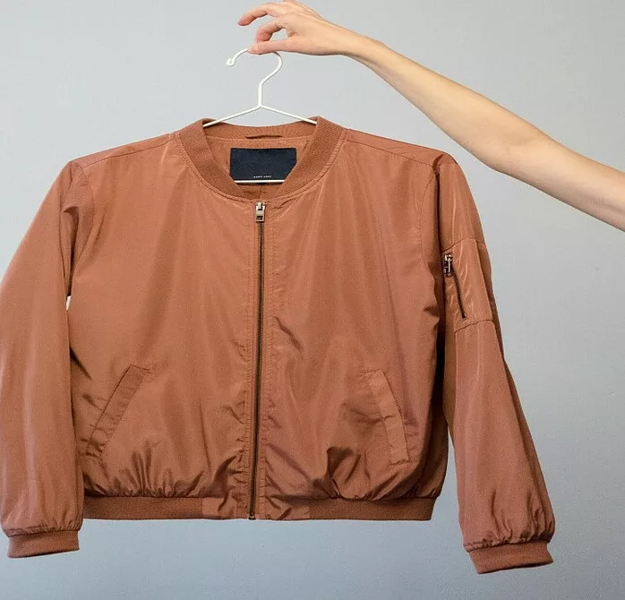 A person holding a hanger with a brown jacket on it.